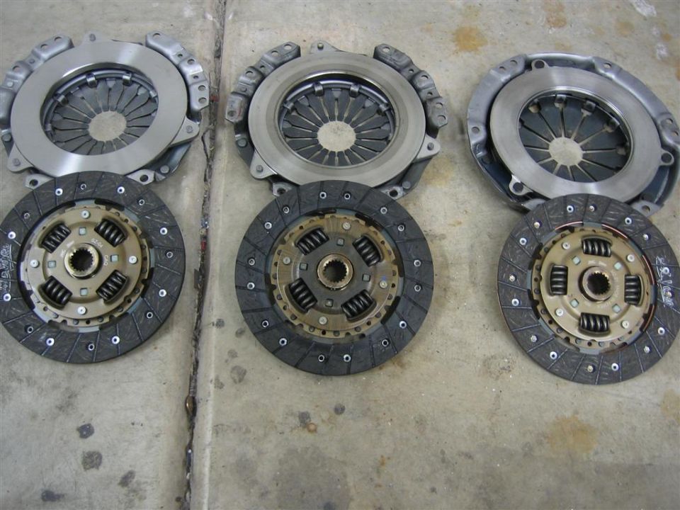 Three clutch kits laid out on a concrete floor. Each kit has a pressure plate and a clutch disc