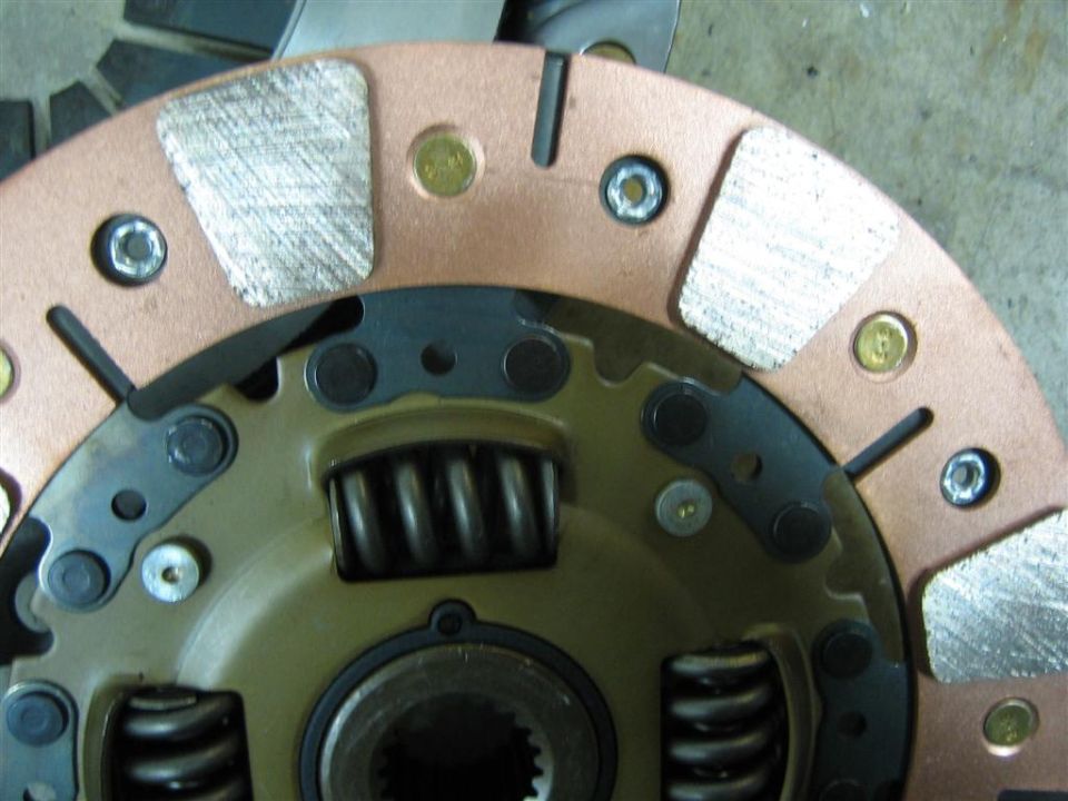 Close-up of copper-colored puck-style clutch disc with damper springs and splined hub on shop floor