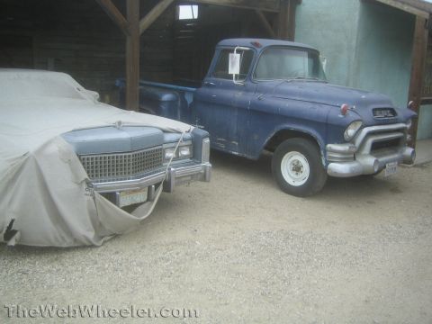 1990 Ford Bronco - weathered blue 1950s GMC pickup truck parked beside a car-covered vehicle under an open wooden shed.