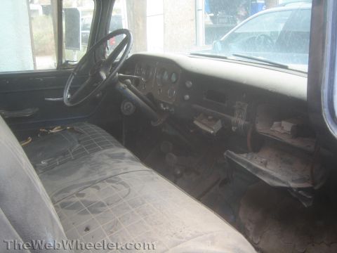 1990 Ford Bronco - dusty, unrestored interior of a vintage truck showing a bench seat, large steering wheel and metal dashboard.