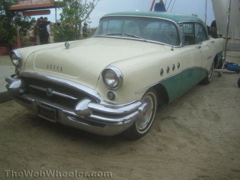 1990 Ford Bronco - two-tone cream and teal 1955 Buick sedan with chrome bumper and portholes parked on sand.