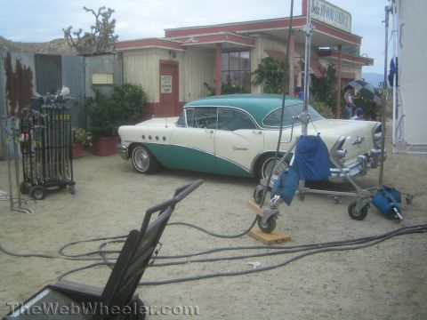 1990 Ford Bronco - two-tone cream and teal 1955 Buick sedan parked on what appears to be a film set surrounded by lighting and grip equipment.