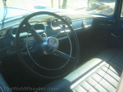 1990 Ford Bronco - Sunlit interior of a vintage car showing a black steering wheel, blue dashboard with gauges and a patterned bench seat.