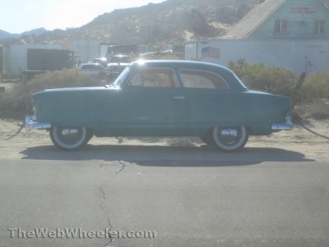 1990 Ford Bronco - Side profile of a teal 1950s Nash compact car with skirted wheels and whitewall tires parked on a desert road.