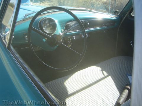 1990 Ford Bronco - Interior of a teal vintage car showing a black steering wheel, round gauge cluster and a checkered cloth bench seat.