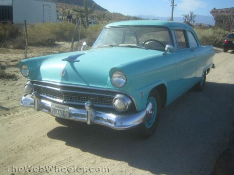 1990 Ford Bronco - Front three-quarter view of a turquoise 1955 Ford two-door sedan with chrome grille and bumper parked on a desert road.