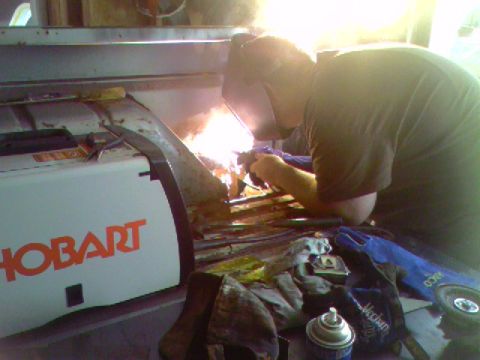 1974 Ford Bronco - A person welds metal components, with a Hobart welding machine and various tools visible in the foreground.