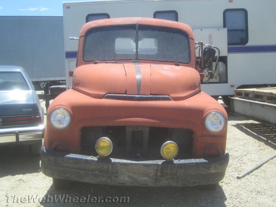 Front view of a faded orange vintage pickup truck in a dirt lot
