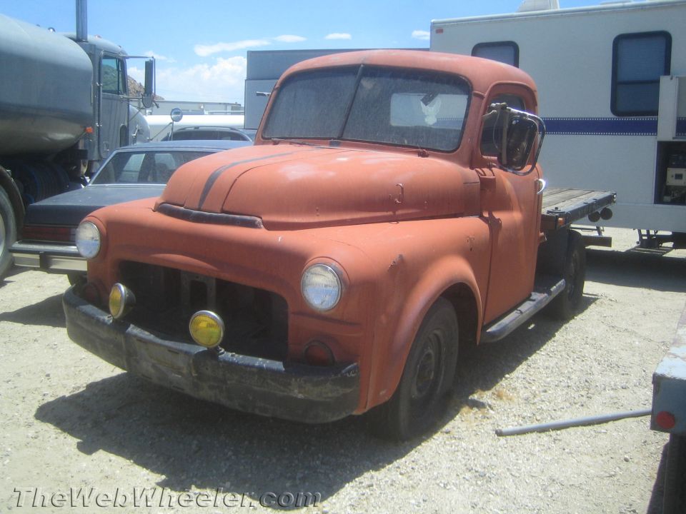Faded orange vintage flatbed pickup truck parked in a gravel yard