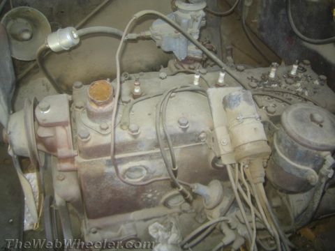 1990 Ford Bronco - dusty, rust-coated inline engine block with carburetor, wiring and accessories, photographed in an engine bay.