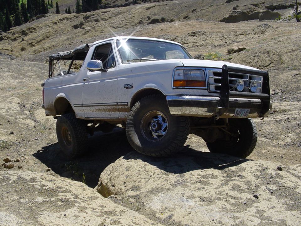 White lifted Ford Bronco with brush guard flexing over rock on a dusty mountain trail