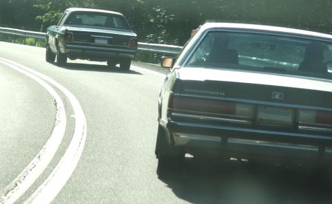 1991 Ford LTD Crown Victoria - Two sedans drive on a highway; the lead car is identified as a Grand Marquis LS.