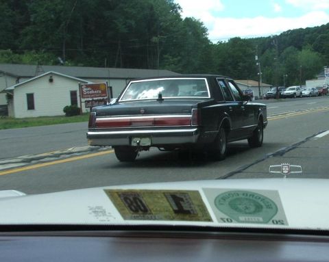 1991 Ford LTD Crown Victoria - A black sedan is seen from behind, displaying a 1980 registration sticker on its windshield, with other vehicles visible in the background.