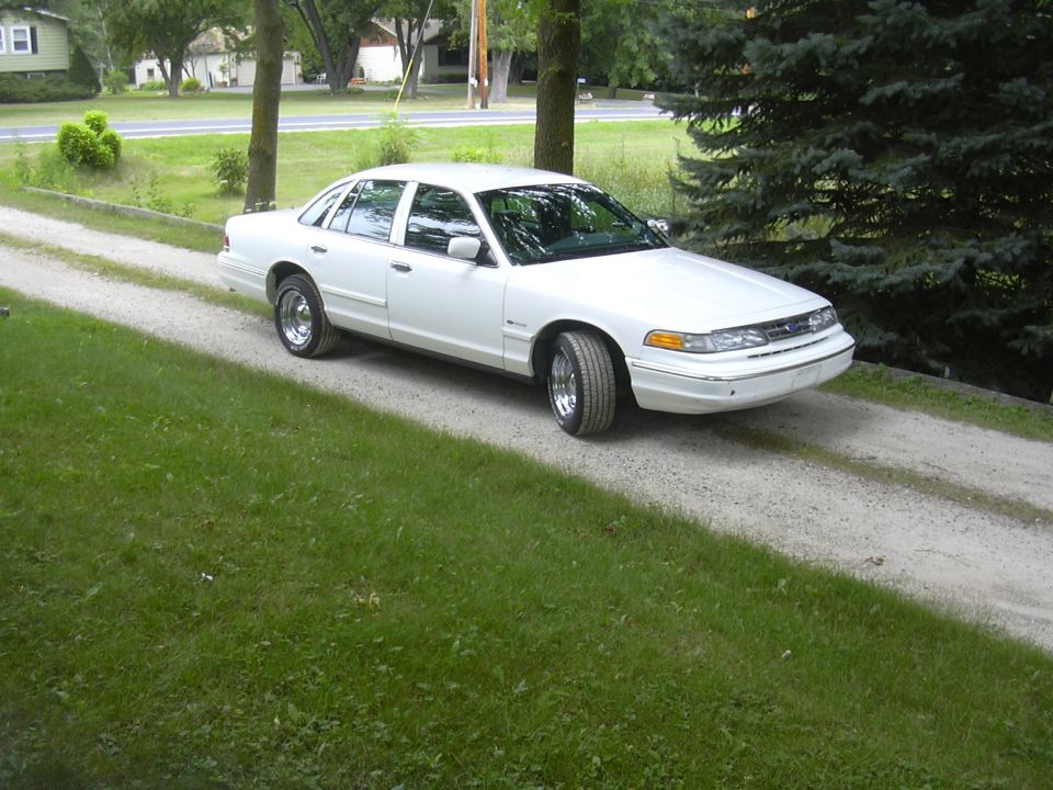 White sedan parked on a gravel driveway. Trees and grass surround the car