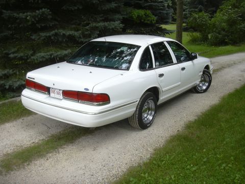 1997 Ford Crown Victoria - A white 1997 Ford Crown Victoria sedan is parked on a gravel driveway with trees in the background.