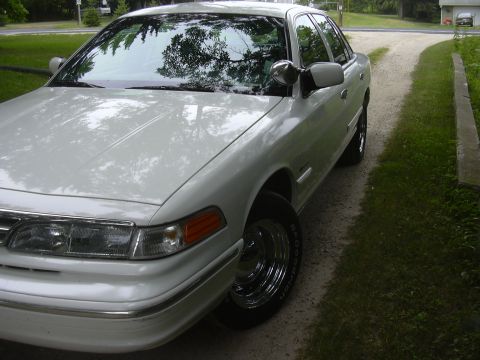 1997 Ford Crown Victoria - This white sedan has a distinctive side mirror and chrome wheels, suggesting it might be a former police vehicle.