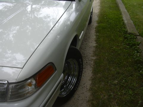 1997 Ford Crown Victoria - A white 1997 Ford Crown Victoria is seen from a low angle, showing its front fender and chrome wheels.