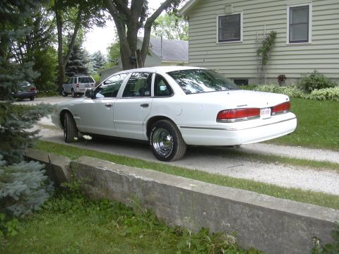 1997 Ford Crown Victoria - A white 1997 Ford Crown Victoria is parked on a gravel driveway in front of a house, with another vehicle visible in the background.