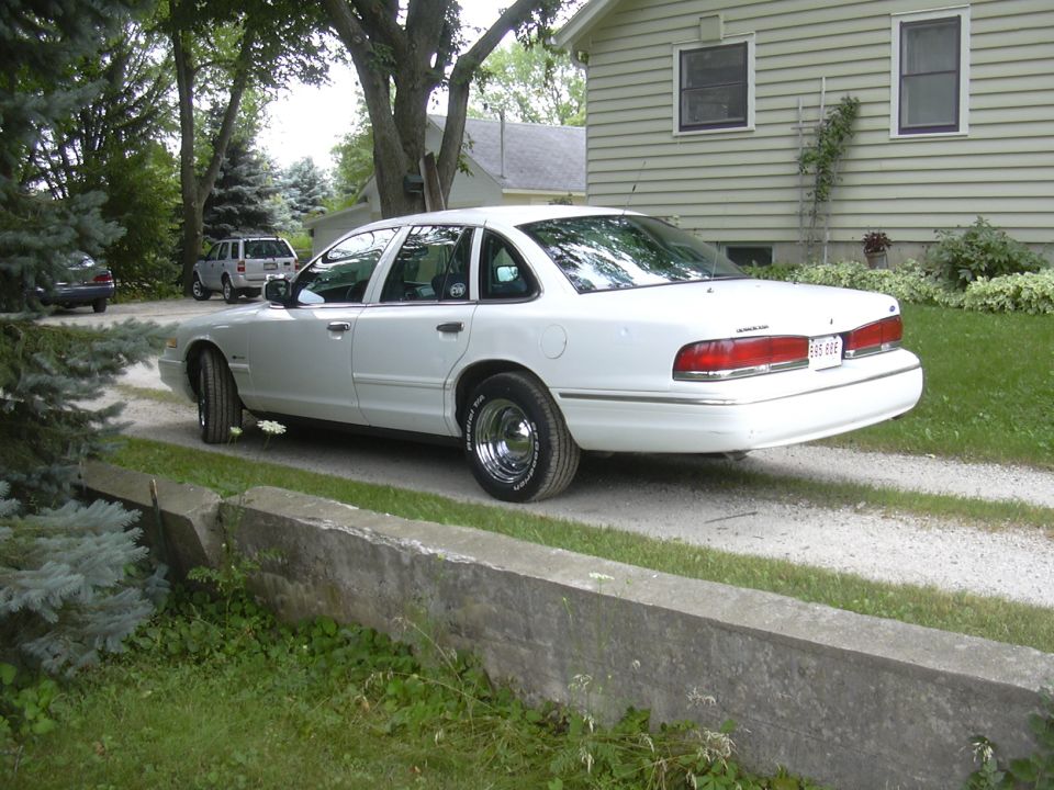 White 1997 Ford Crown Victoria parked on a gravel driveway next to a house