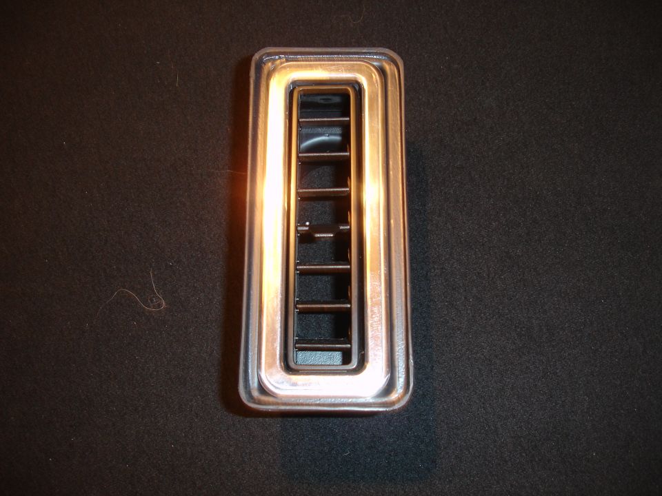 Chrome-trimmed rectangular air vent with horizontal slats against a dark textured background