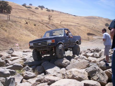 1989 Ford Bronco - A lifted Ford truck navigates a rocky off-road course under a clear blue sky.