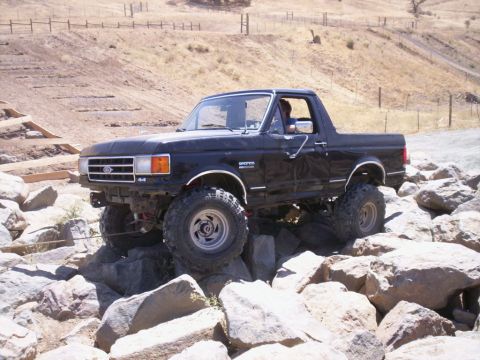1989 Ford Bronco - This black Ford Bronco is shown off-roading on a challenging rocky course.