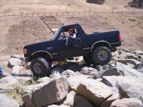 1989 Ford Bronco - A black Ford Bronco navigates a rocky obstacle course on a dry, grassy hillside.