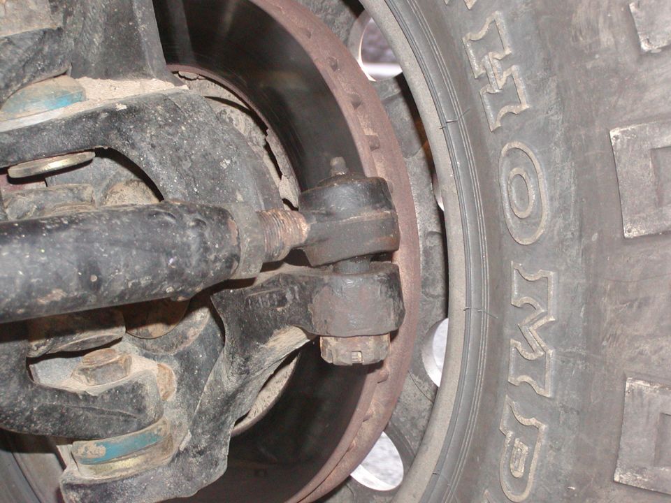 Close-up of a vehicle's steering linkage, tie rod end, brake rotor, and tire tread