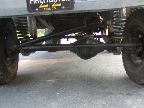 1991 Ford Bronco - Close-up view of the steering and suspension system, showing the differential and tie rods. A "FIREFIGHTER" license plate frame is visible.