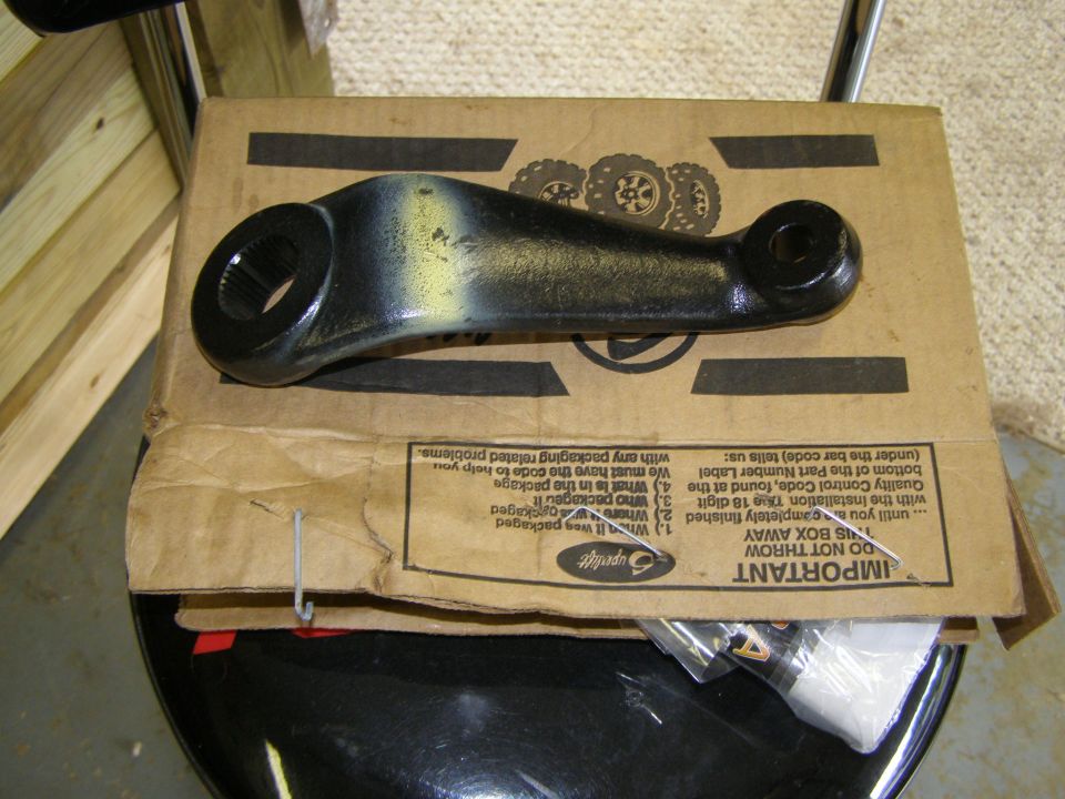 Black steering linkage part with yellow markings on a cardboard box