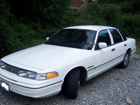 1994 Ford Crown Victoria - This white sedan, likely a 1992 model, is viewed from the front three-quarter angle on a gravel surface.