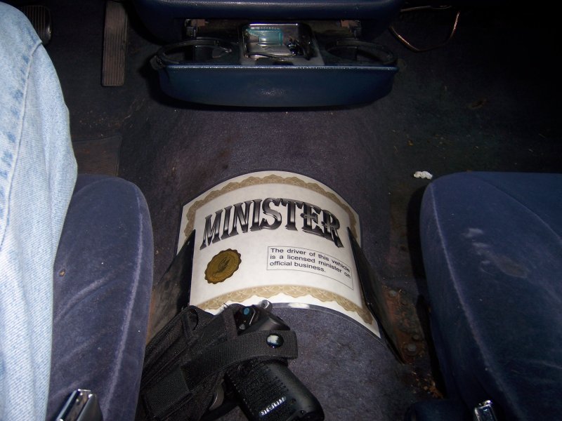 Car interior showing minister certificate on the floor and a handgun on the seat