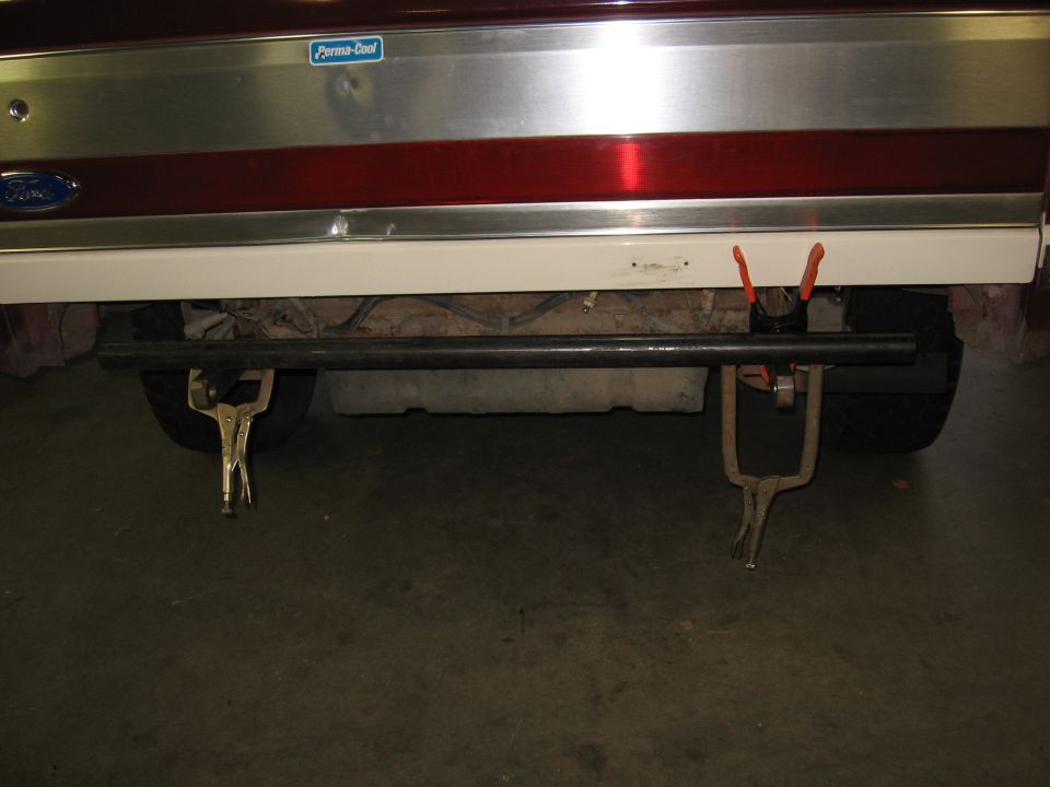 Ford emblem on red and silver tailgate with clamps holding a metal bar for bumper fabrication