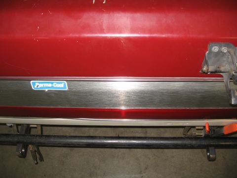 1991 Ford Bronco - Close-up of a red vehicle's rear bumper, a chrome trim strip with a 'Perma-Cool' sticker.