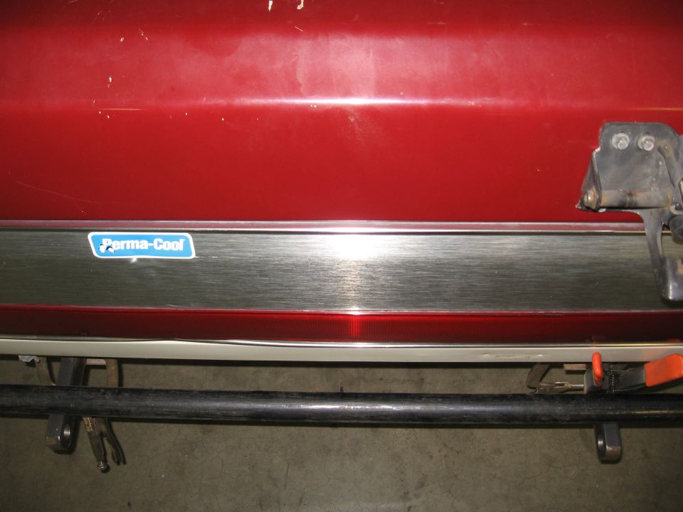 Red vehicle rear bumper with chrome trim and 'Perma-Cool' sticker, showing part of a black bar below