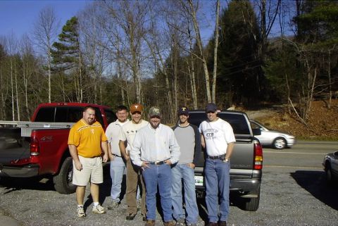 1995 Ford Bronco - A group of friends pose with their trucks on a sunny day, with a silver car driving by on the road.