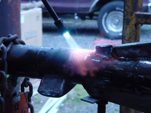 1979 Ford Bronco - A torch heats a metal component, with chains visible on the left and a vehicle in the background.