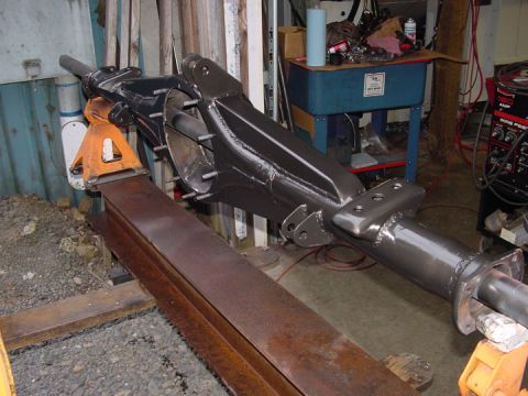1979 Ford Bronco - A gray painted axle assembly is supported by jack stands and steel beams in a workshop.