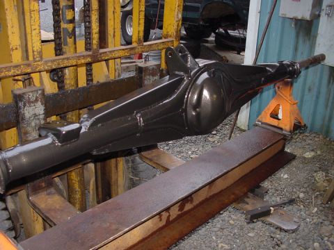 1979 Ford Bronco - A freshly painted rear axle assembly is supported by jack stands, with a forklift and another vehicle visible in the background.
