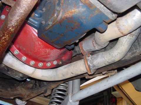 1979 Ford Bronco - Close-up of a vehicle's exhaust system and differential cover, showing rusted metal components.