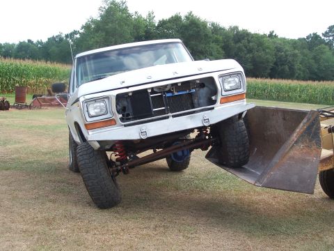 1979 Ford Bronco - A white 1979 Ford Bronco is equipped with a front loader attachment, modified with a custom bumper and visible radiator.