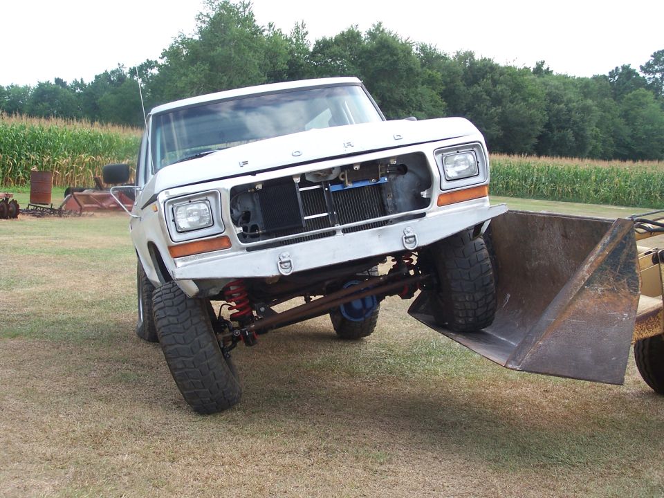 White 1979 Ford Bronco with front loader attachment, angled front view, showing custom bumper and exposed radiator