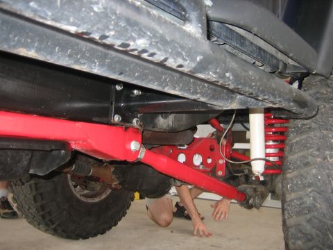 2001 Jeep Wrangler - Close-up view of the undercarriage of a Jeep, highlighting suspension upgrades and a mechanic's work.