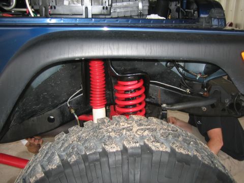 2001 Jeep Wrangler - Close-up of the suspension system on a blue Jeep Wrangler, showing red coil springs and shocks.