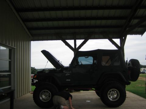 2001 Jeep Wrangler - A person works on a dark green 2001 Jeep Wrangler parked under a covered structure.