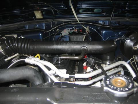 2001 Jeep Wrangler - The engine compartment of a Jeep shows various hoses, wires, and the radiator cap.