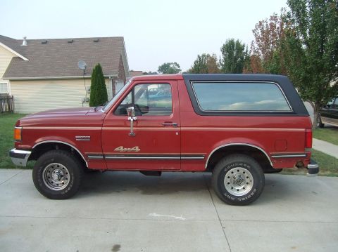1987 Ford Bronco - This red 1987 Ford Bronco features a black removable top and prominent 4x4 badging on its side.