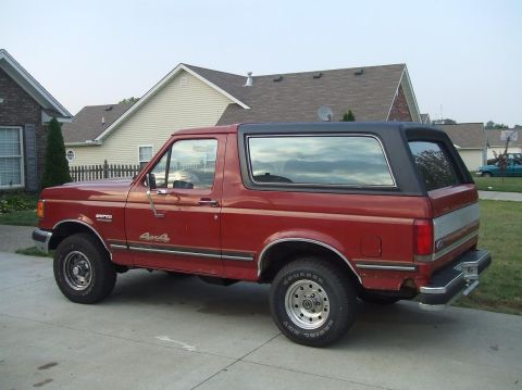1987 Ford Bronco - Side view of a red 1987 Ford Bronco 4x4 parked in front of a suburban house.