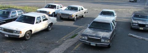 1991 Ford LTD Crown Victoria - A collection of sedans, including a white 1991 Ford Crown Victoria LTD, are parked together in a lot.
