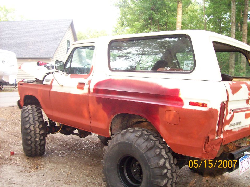 Lifted Ford Bronco in red primer with white hardtop on oversized tires on a gravel driveway